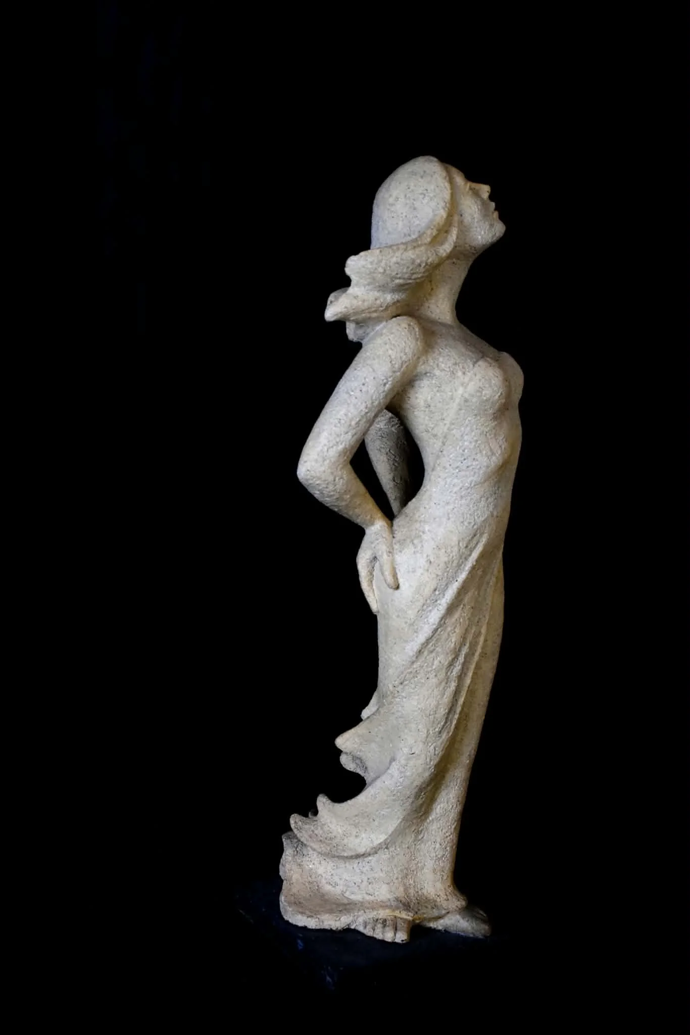 Sculpture d’une femme debout en pierre claire, sur fond noir