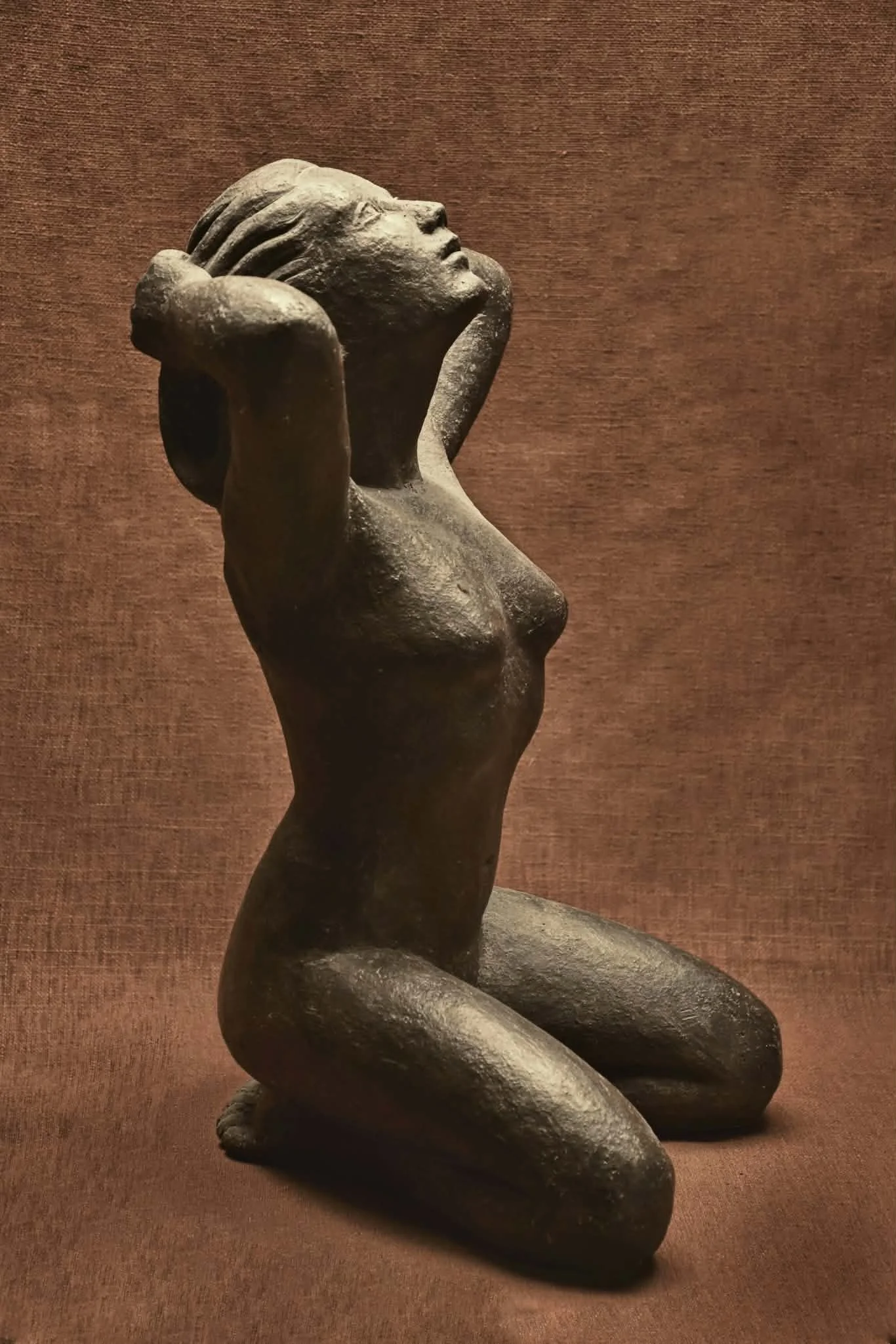 Sculpture d’une femme agenouillée, bras levés derrière la tête