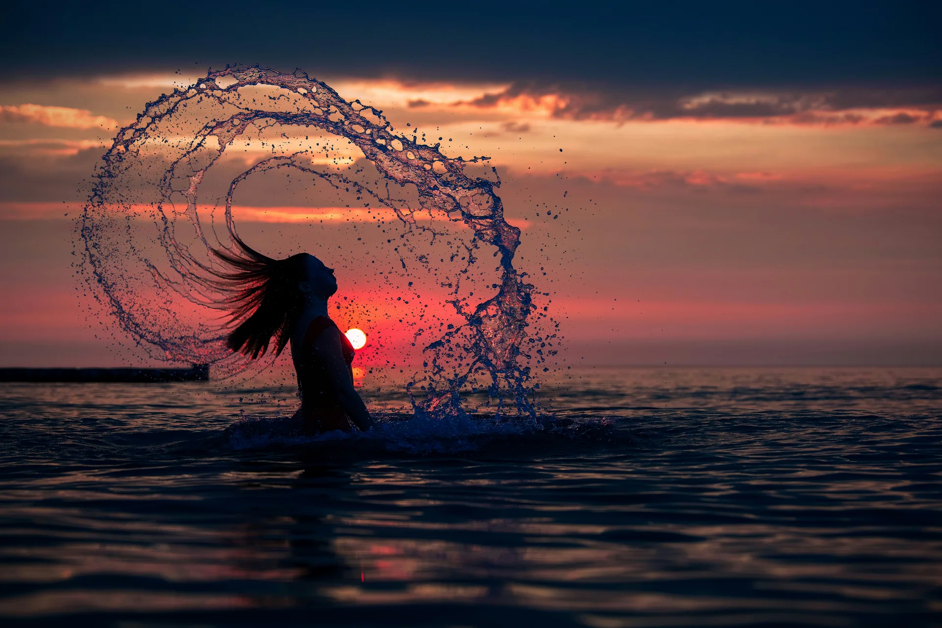 Silhouette d’une personne faisant tournoyer ses cheveux mouillés au coucher du soleil