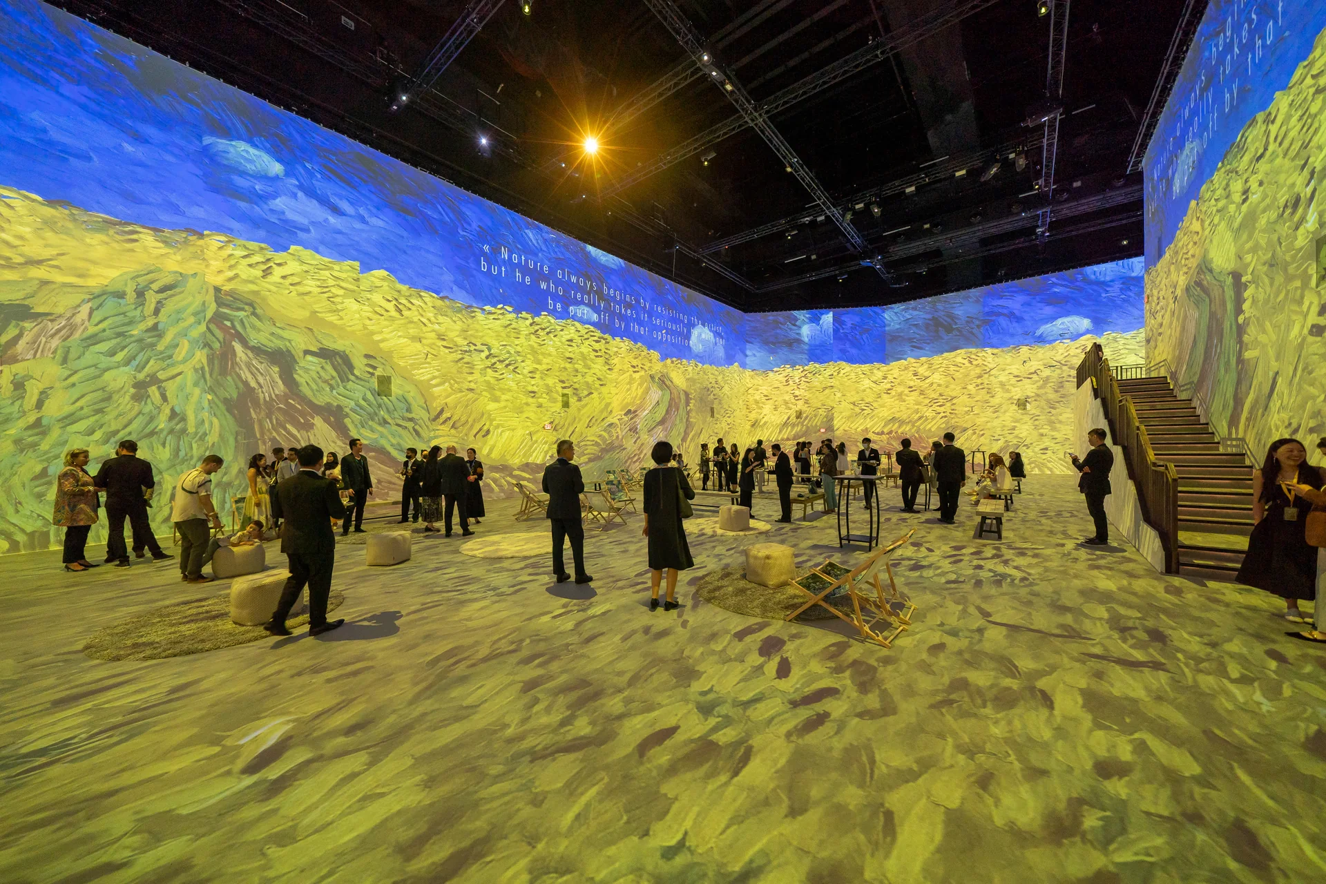 Visiteurs dans une grande salle immersive où les champs de blé de Van Gogh sont projetés sur les murs et le sol
