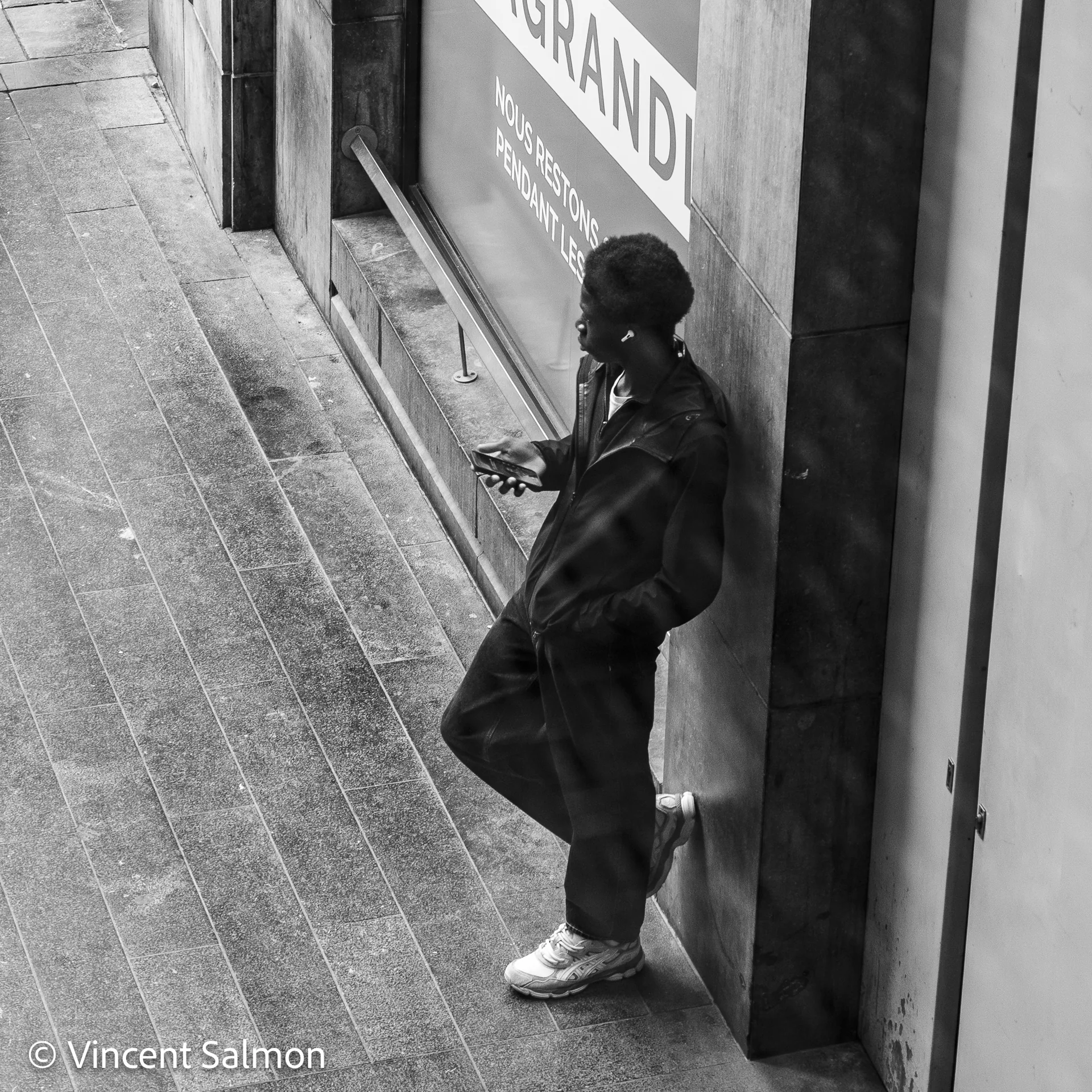 Photo de Vincent Salmon : une silhouette appuyée contre un mur, téléphone en main