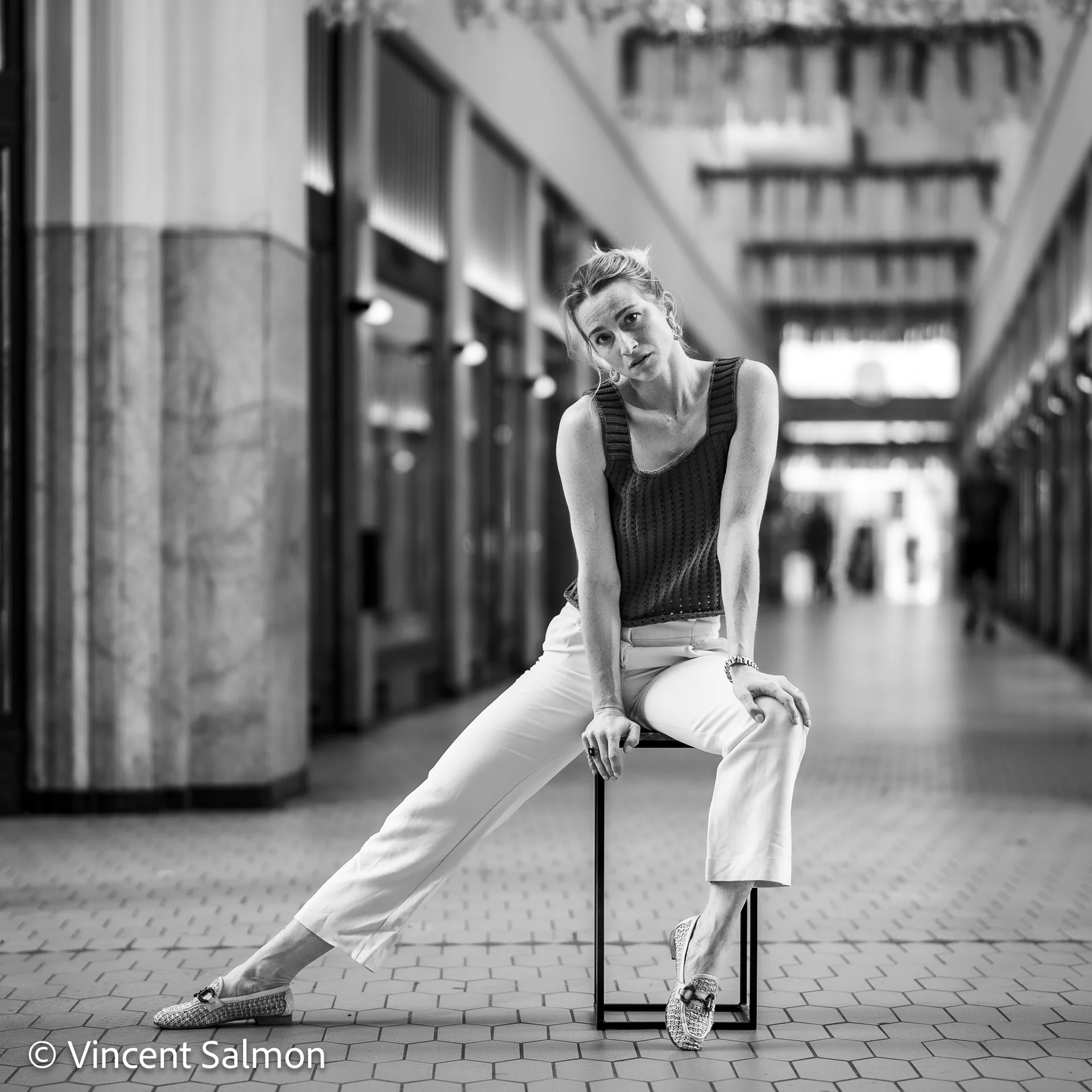 Photo de Vincent Salmon : une femme assise sur un tabouret dans une galerie commerçante, en noir et blanc