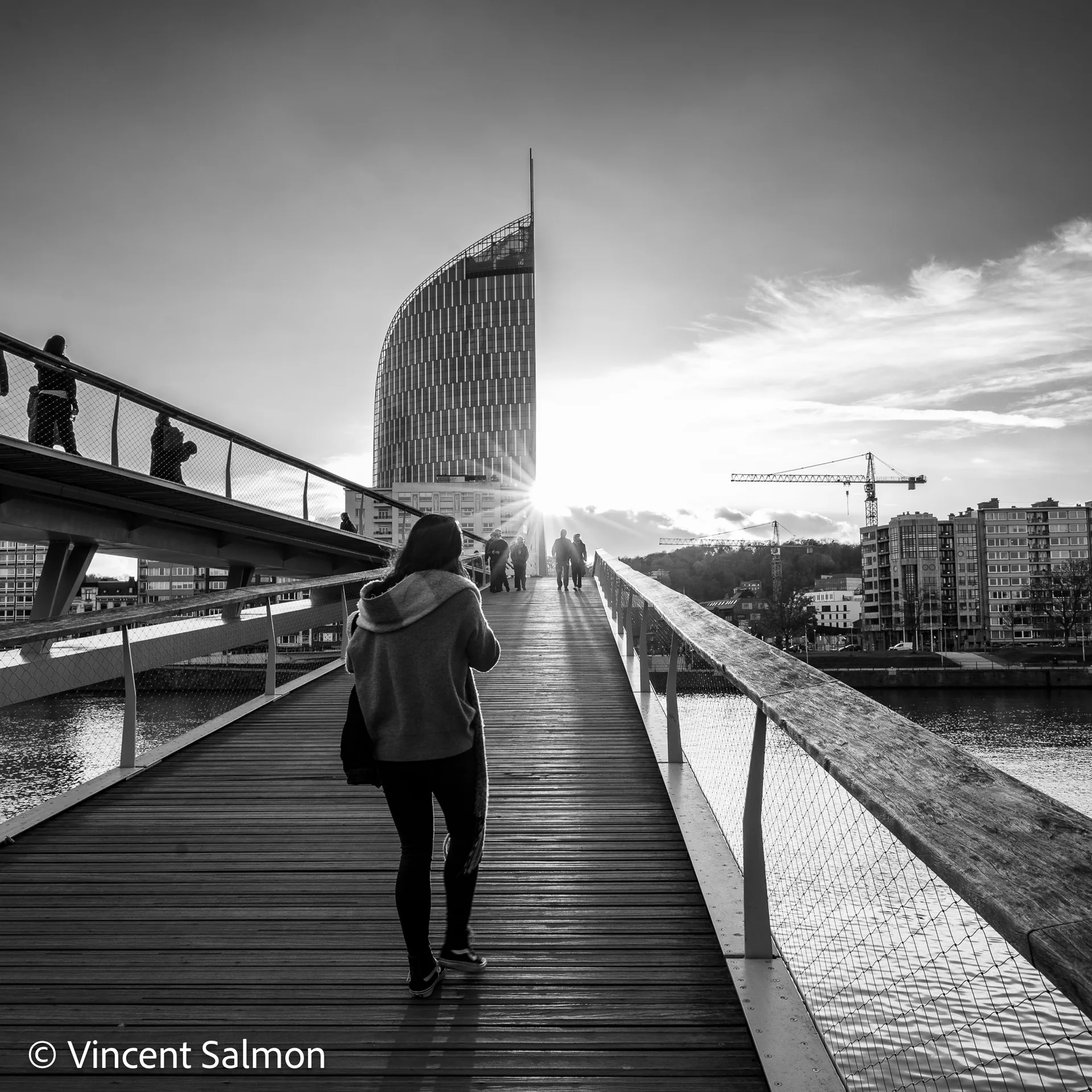 Photo de Vincent Salmon : une passante sur une passerelle face à une tour, à contre-jour