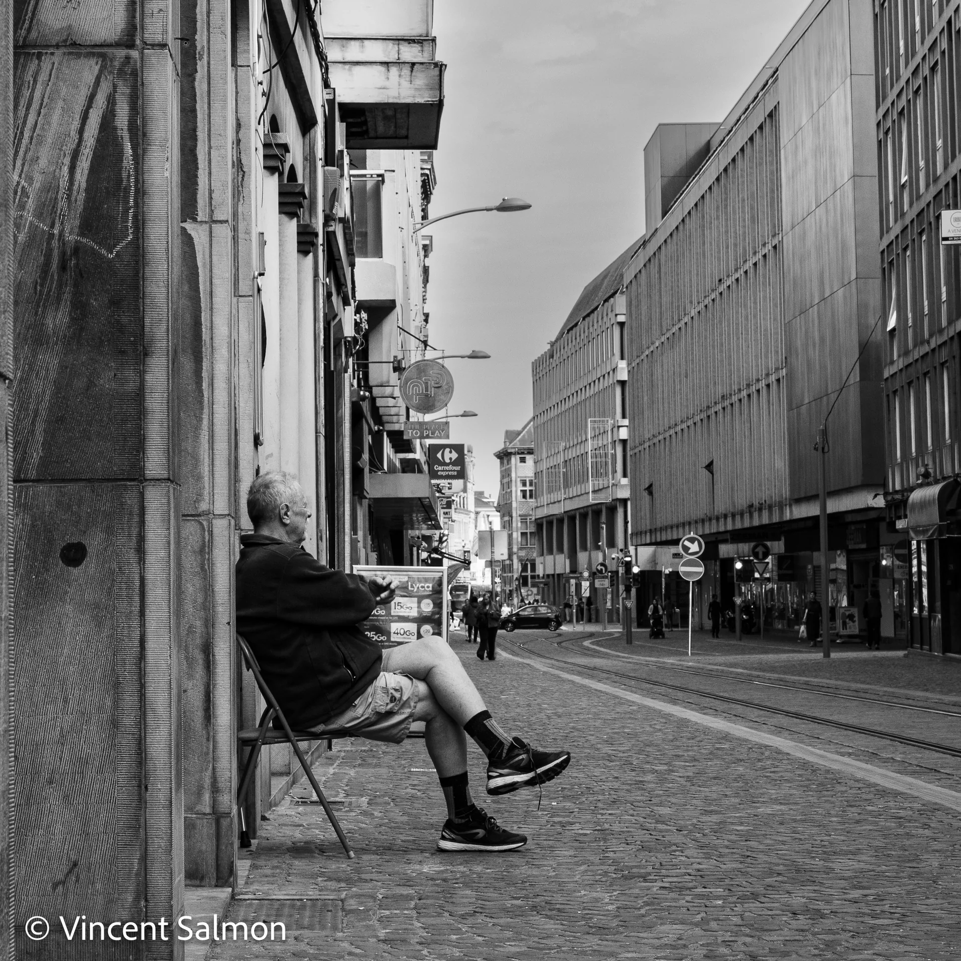 Photo de Vincent Salmon : un homme assis sur une chaise pliante au bord d’une rue