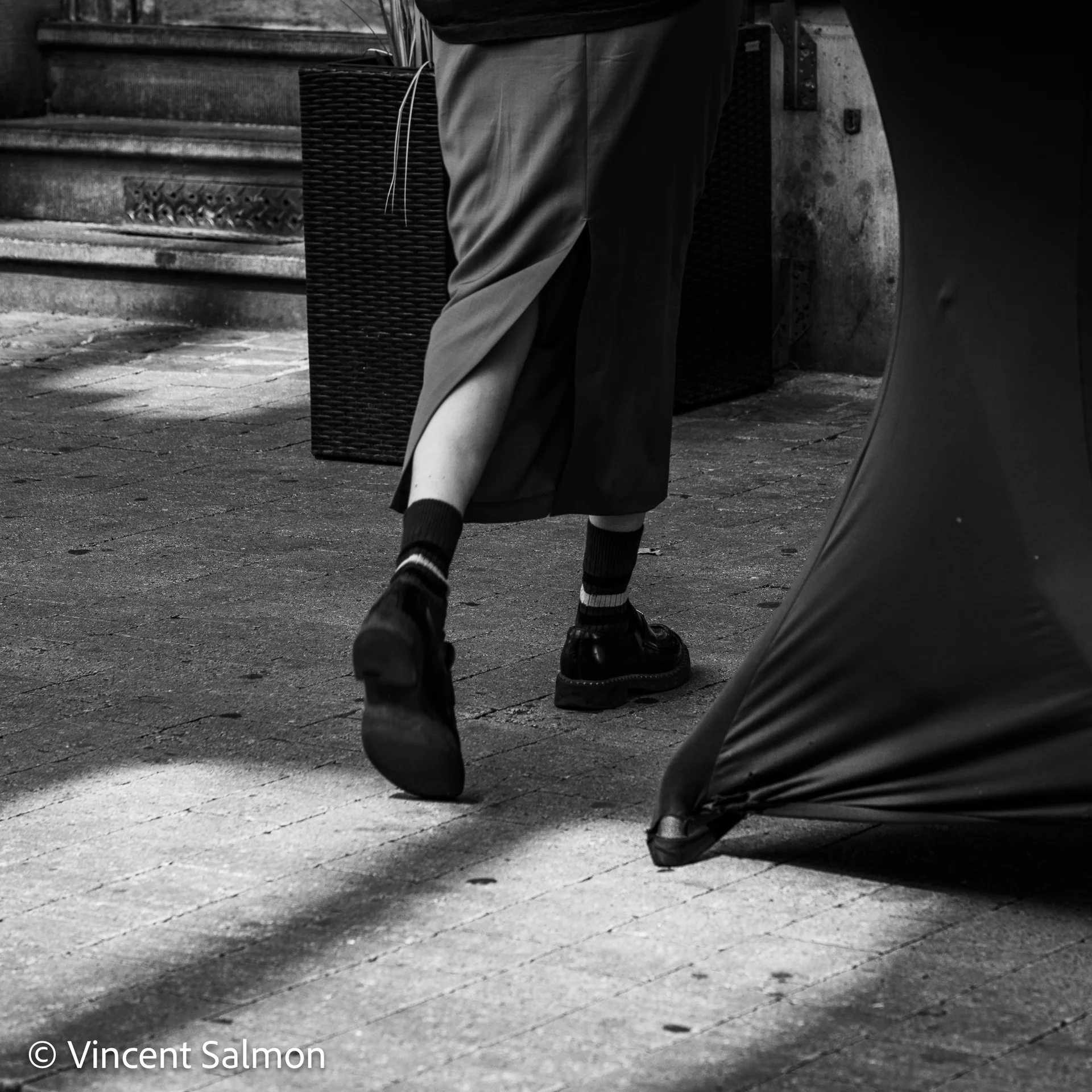 Photo de Vincent Salmon : les jambes d’un passant et un pan de tissu sur un trottoir